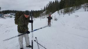 Yksi hiihtäjä lähtenyt taukopaikalta, toinen puhdistaa kertynyttä lunta suksen alta.
