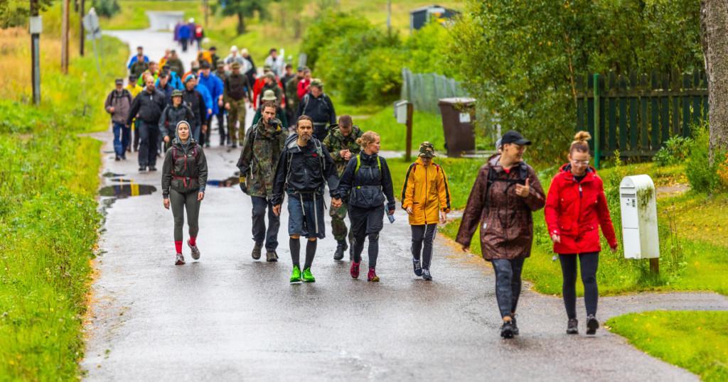 Kesäyön marssin osallistujat kävelevät sateisella tiellä kohti kameraa.