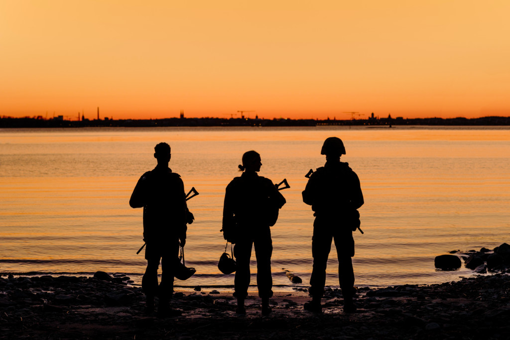 Kuvituskuva kolme sotilasta auringonlaskussa rannalla