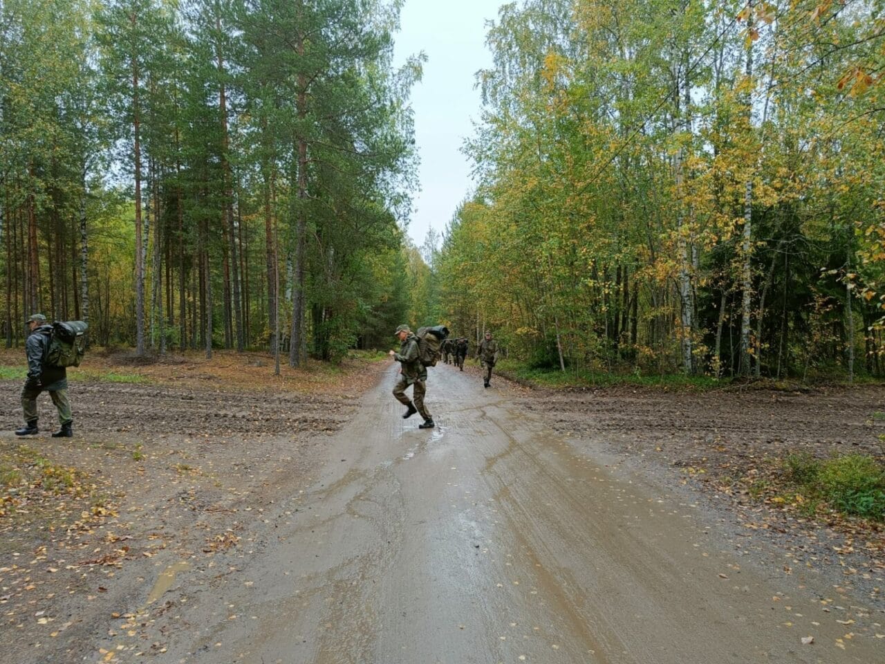 Ryhmä maastopukuisia ihmisiä ylittää metsäistä tietä