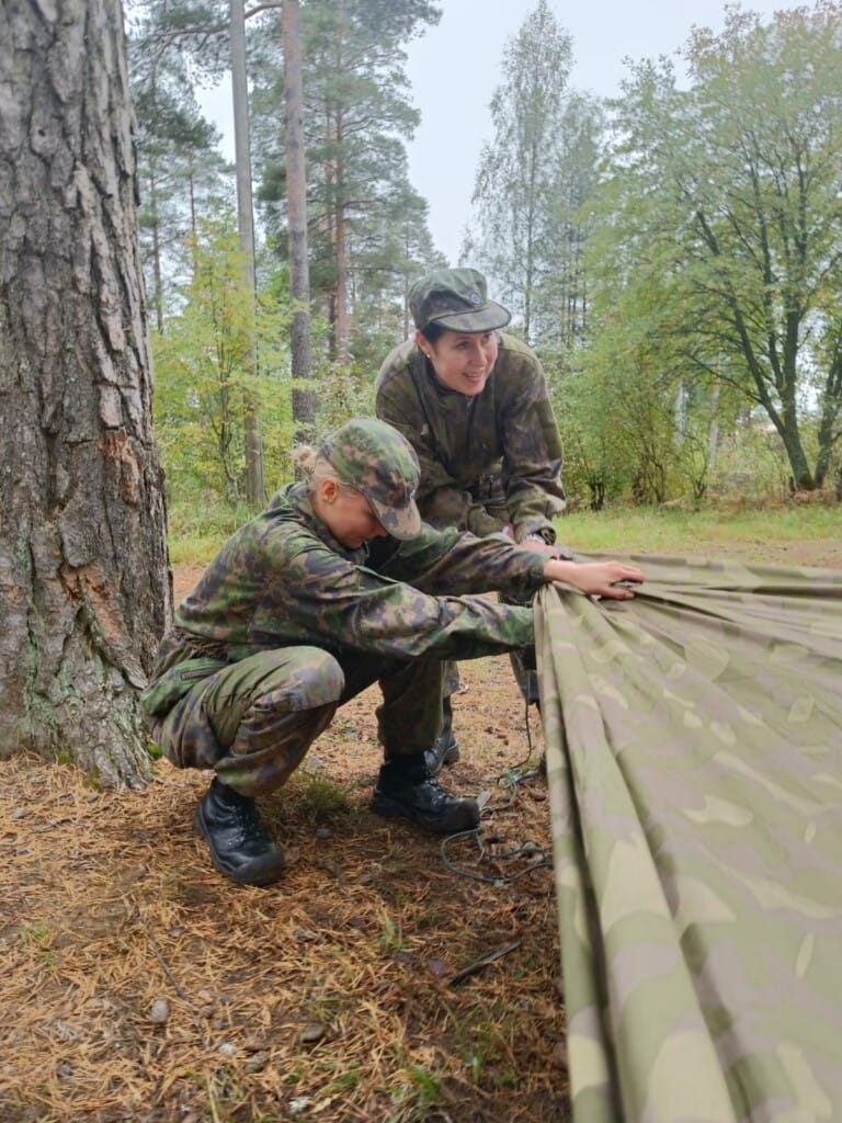 Kaksi naista virittää metsässä telttaa