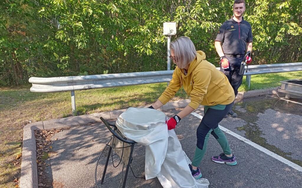 Nainen sammuttaa grillipaloa sammutuspeitteellä. Taustalla mies pelastuslaitoksen asussa.