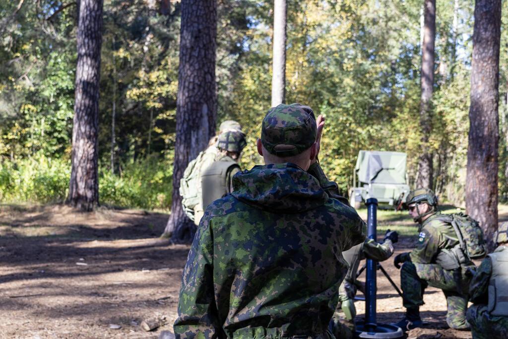 Maastopukuinen upseeri kohdistamassa edessä olevan kranaatinheittimen miehistön tuliasemaa.