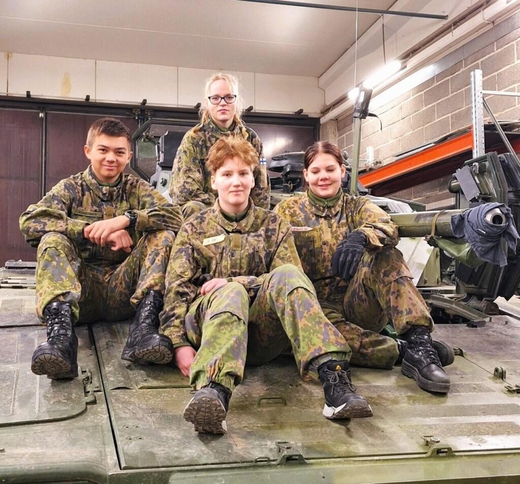 Neljä nuorta maastopuvuissa panssarivaunun päällä istumassa.