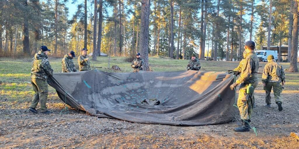 Nuoret pystyttävät puolijoukkuetelttaa metsässä.