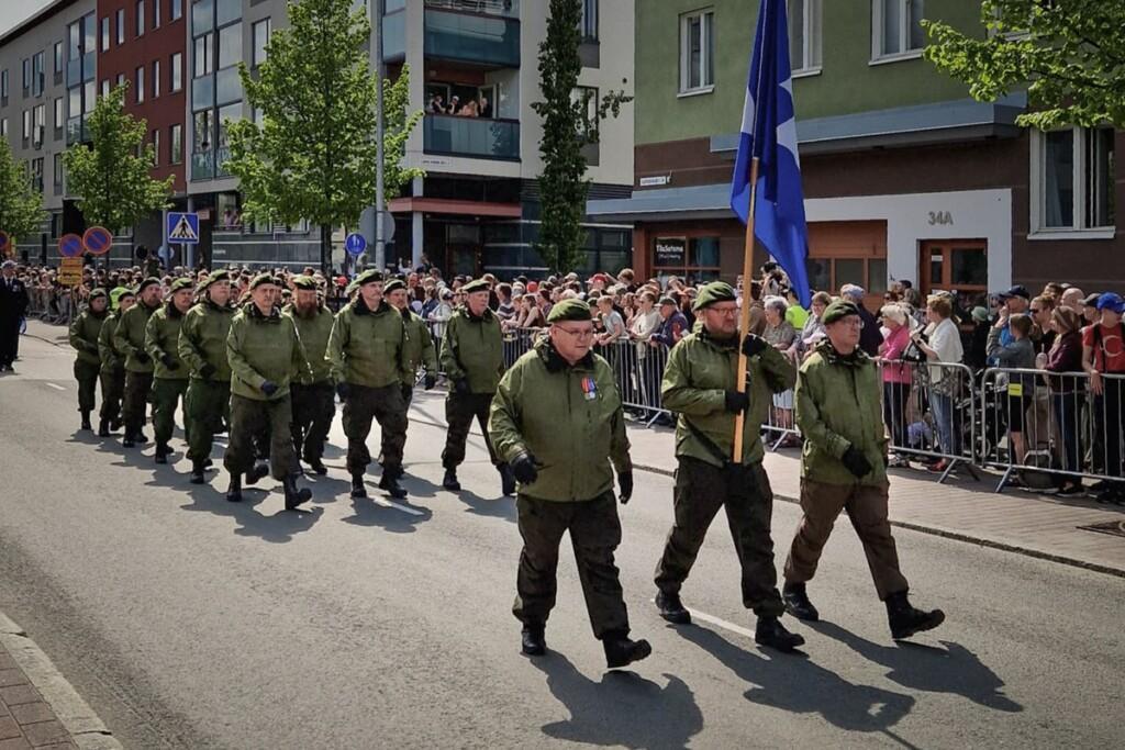 Vihreissä MPK-asuissa marssiva joukko kaupunkimaisemassa.
