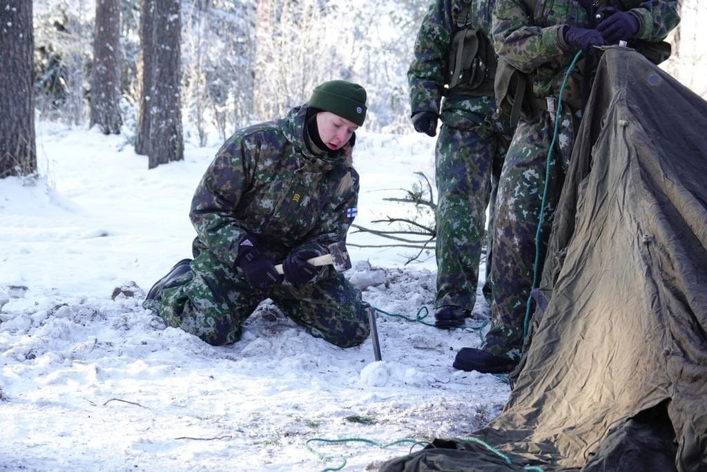 Nainen lyö telttakiilaa jäiseen maahan.