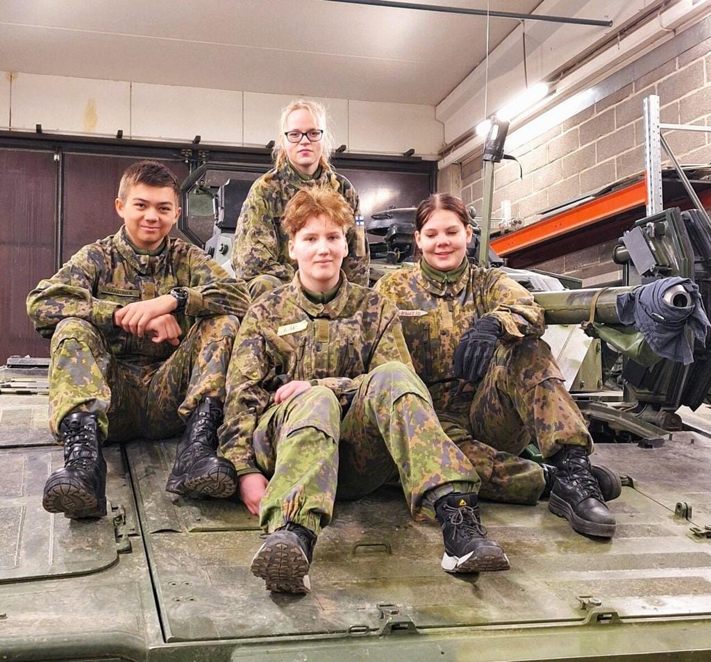 Neljä nuorta maastopuvuissa panssarivaunun päällä istumassa.