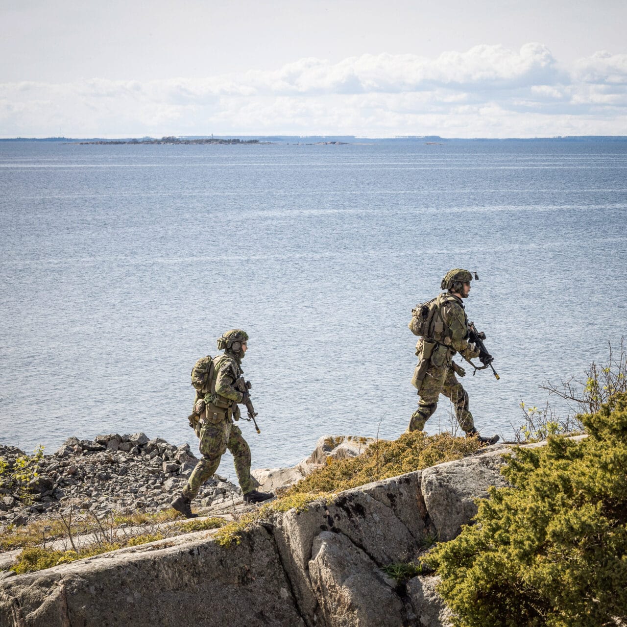 Kaksi sotilaspukuista henkilöä kävelee rantakalliolla