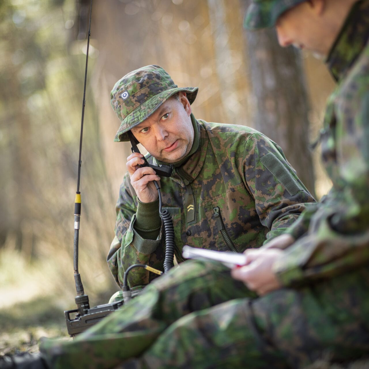 Maastopukuinen henkilö soittaa kenttäpuhelimella