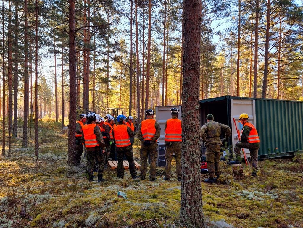 Ryhmä huomioliivisiä henkilöitä metsässä kontin luona