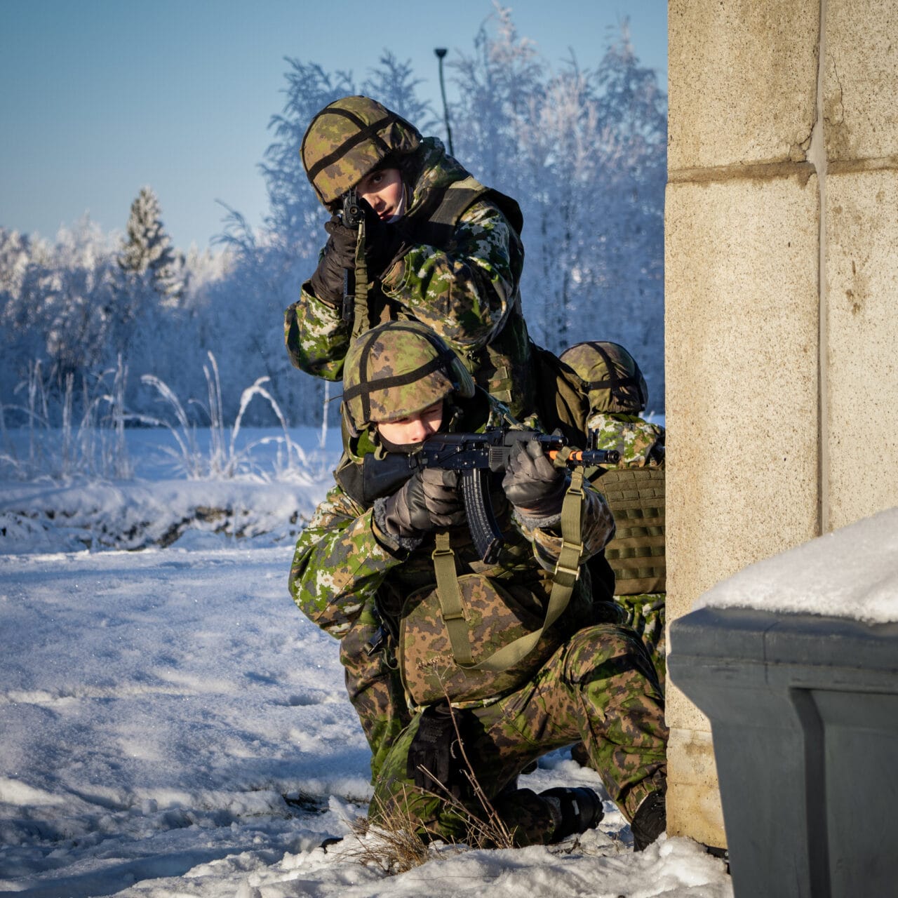 Kaksi sotilaspukuista henkilöä talon nurkalla aseineen