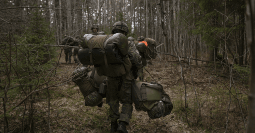 Reserviläisiä kävelemässä metsässä kantaen reppuja ja muita varusteita.