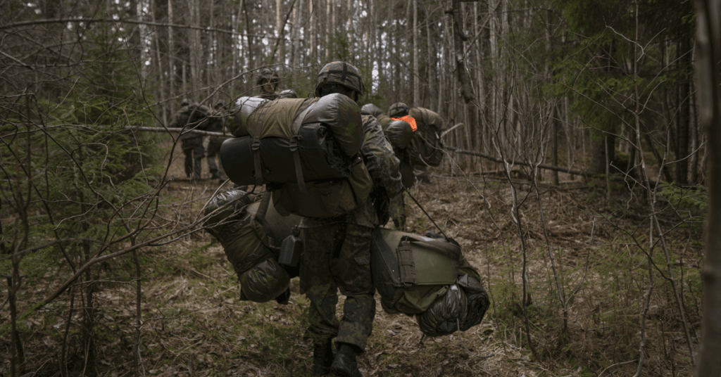 Reserviläisiä kävelemässä metsässä kantaen reppuja ja muita varusteita.