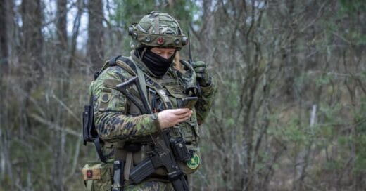 Maastopukuinen henkilö katsoo kädessään olevaa kännykkää.
