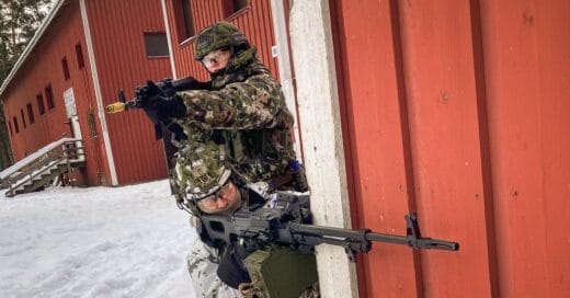 Kaksi sotilaspukuista henkilöä aseet kädessään tähtäilevät talon nurkalla
