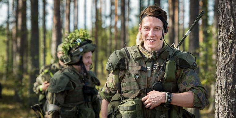 Kolme iloista henkilöä metsässä. Kaikilla maastopuku yllään.