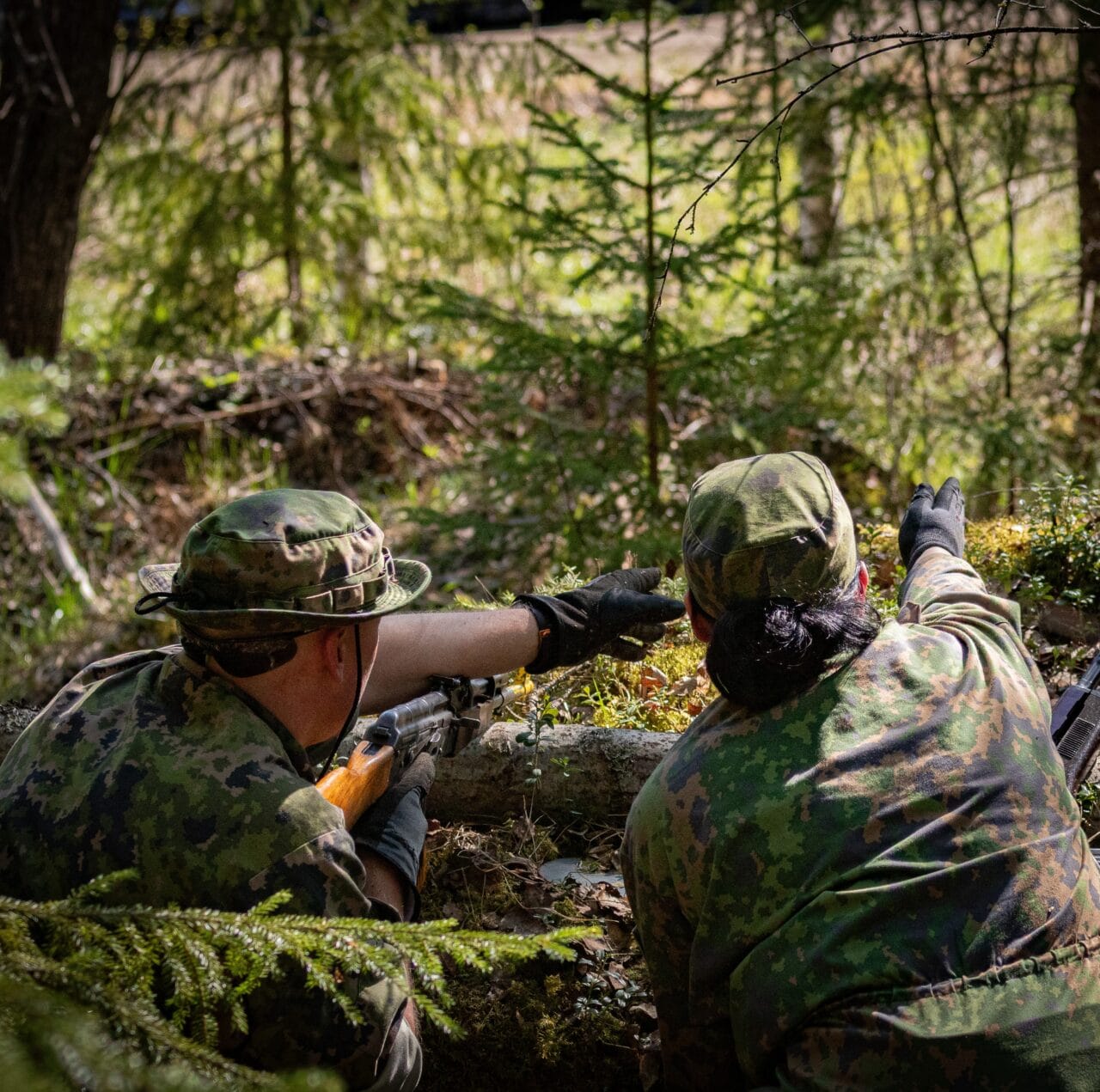 Kaksi henkilöä maastopuvuissa tähyilee metsään maahan kaivetussa kuopassa.