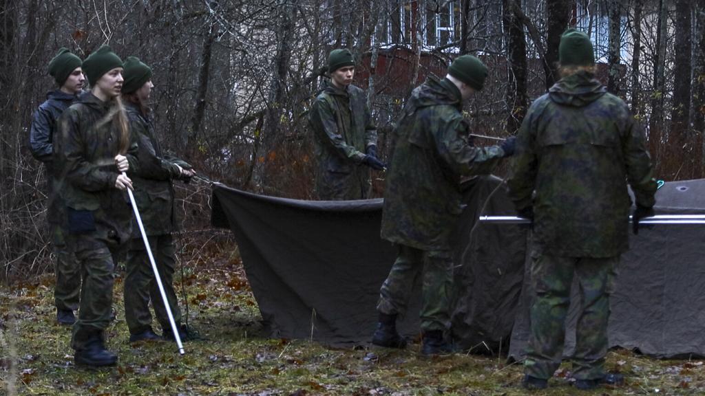 Nuoret pystyttämässä telttaa maastopuvuissa.