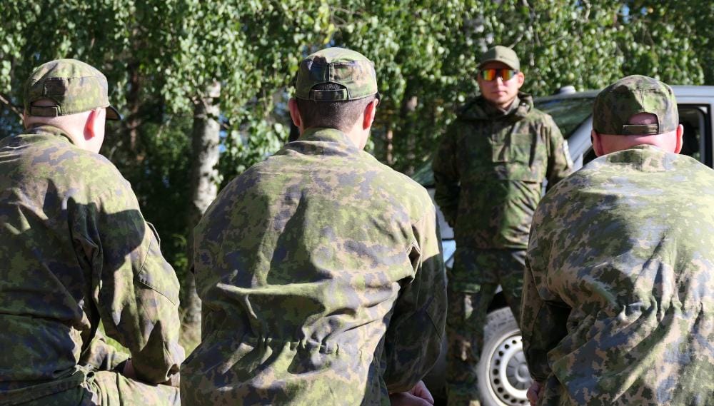 Maastopukuiset henkilöt kuuntelevat ohjaajaa