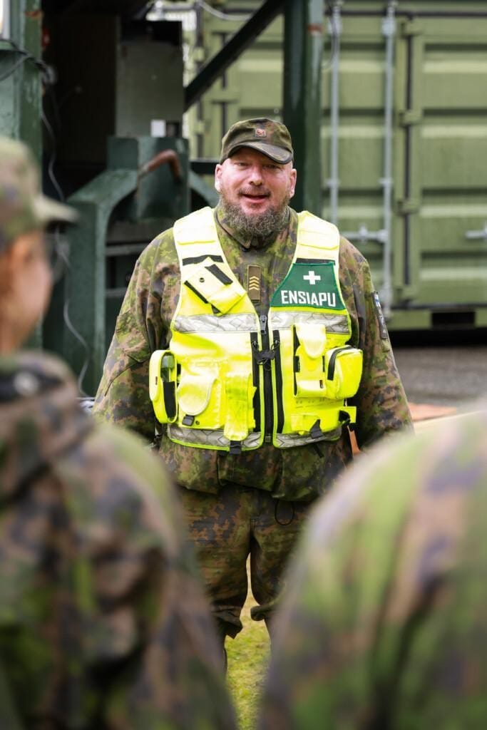 Maastopukuun ja heijastinliiviin pukeutunut mies seisoo yleisön edessä.