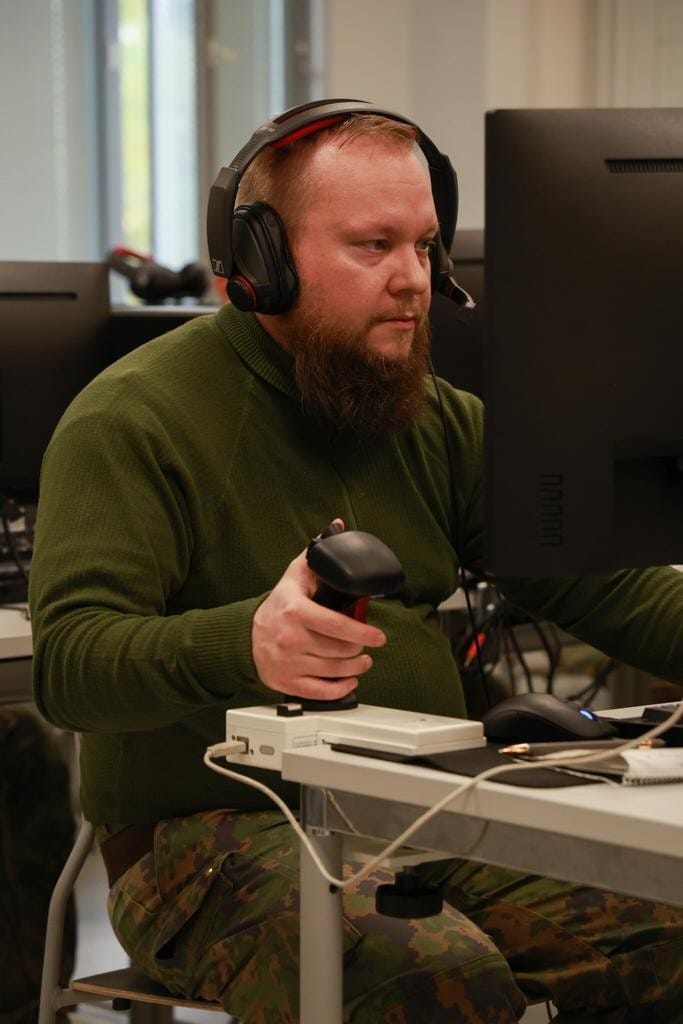 Vihreäpaitainen parrakas mies istuu tietokoneen ääressä kuulokkeet päässään.