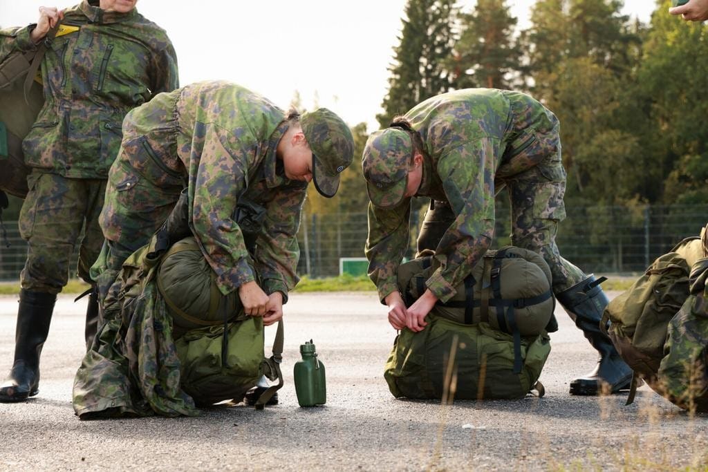 Kaksi maastopukuun pukeutunutta naista pakkaa reppujaan asfaltilla.