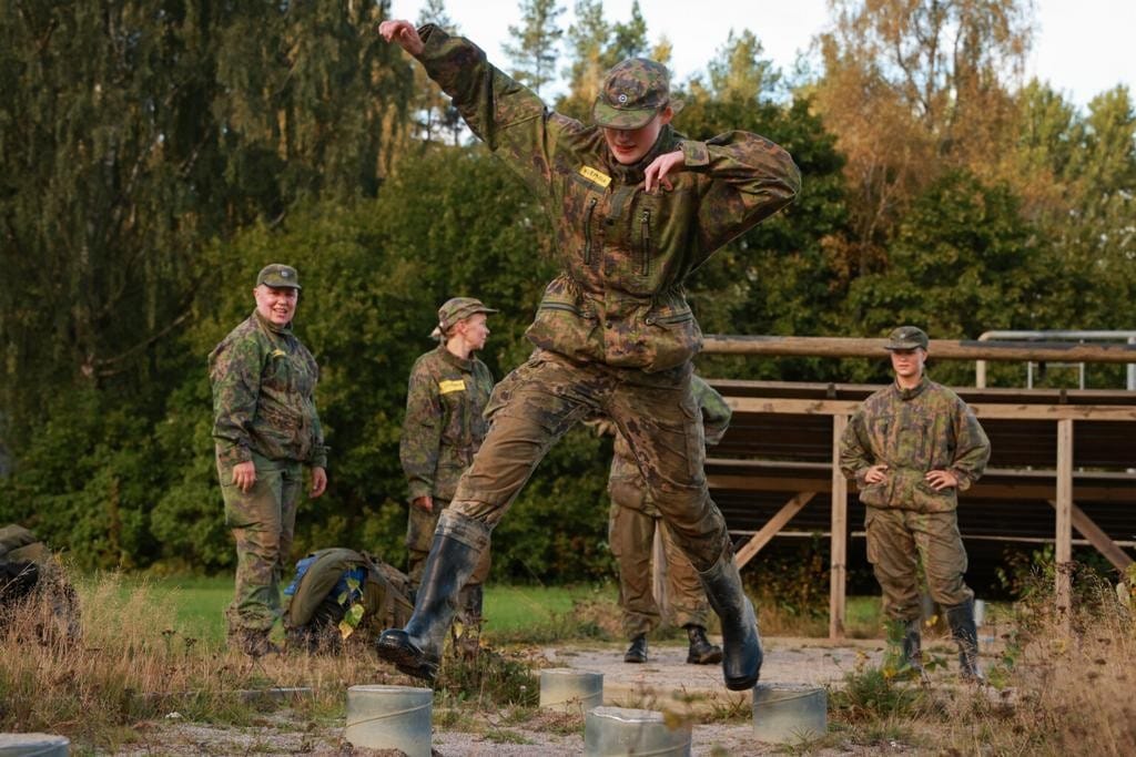 Maastopukuun pukeutunut nainen hyppelee betoniesteeltä toiselle.