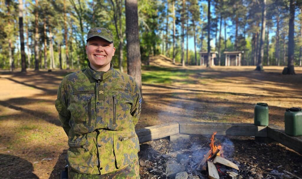 Sotilaspukuinen nainen hymyilee nuotion äärellä