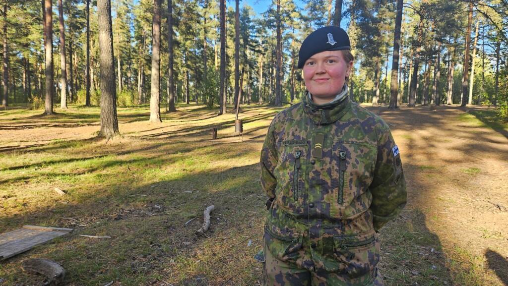 Sotilasasuinen nainen hymyilee metsässä