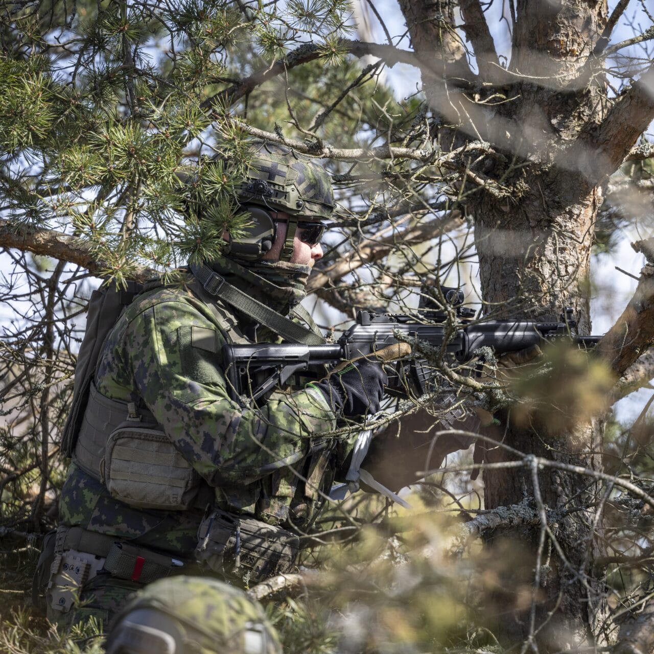 Sotilasasuinen henkilö ase kädessä puustossa
