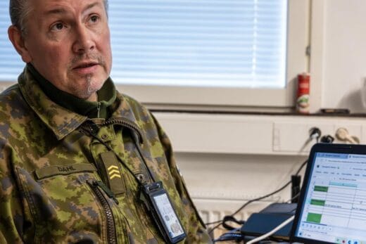Kuvassa on maastopukuun pukeutunut mies, jonka vieressä pöydällä on avoinna kannettava tietokone.