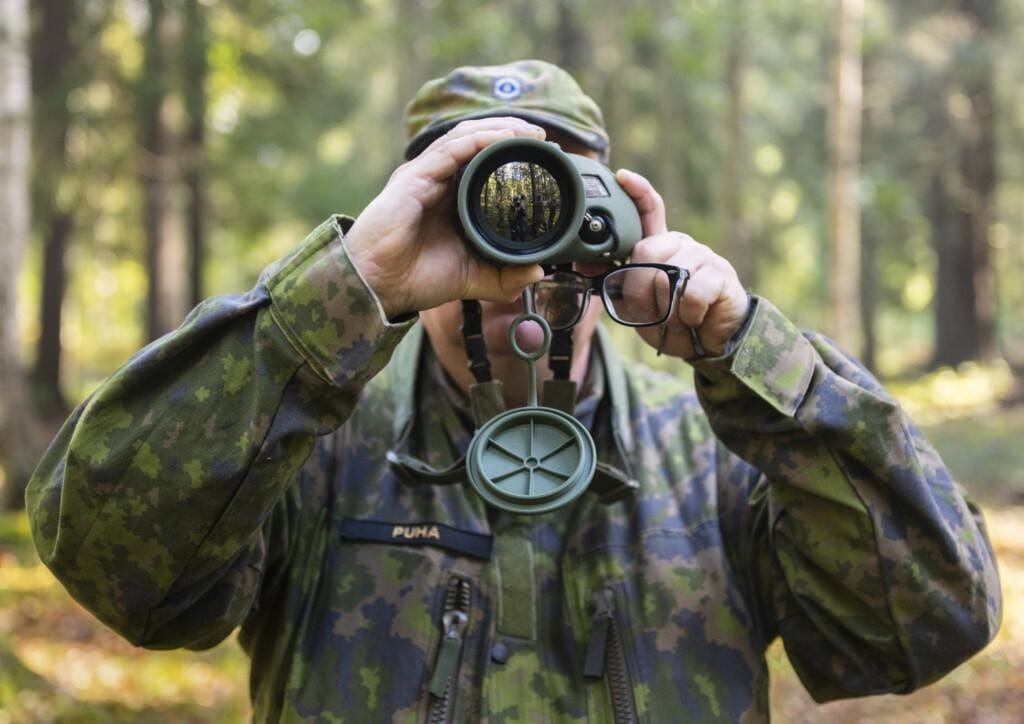 Sotilas tähystää suoraan kameraan. Kameran linssistä heijastuu kuvaaja.