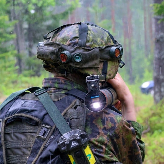 Sotilaspukuinen henkilö takaapäin kuvattuna metsässä
