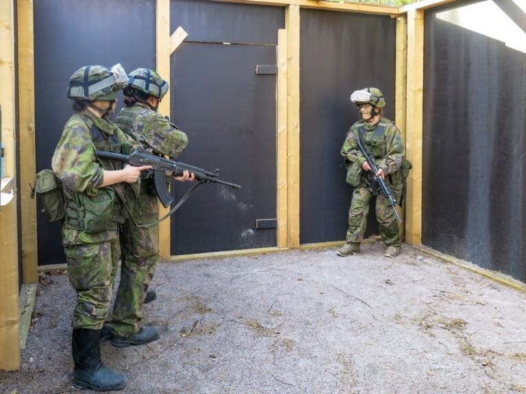 Kolme sotilaspukuista henkilöä aseet kädessä oven edessä