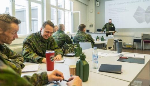 Maastoasuisia henkilöitä luokassa seuraamassa luentoa