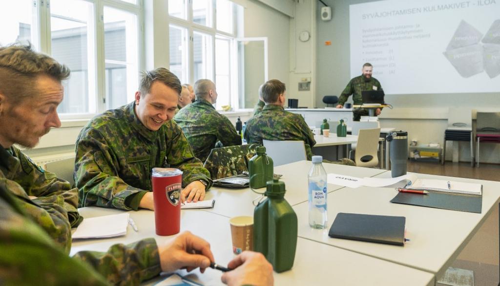 Maastoasuisia henkilöitä luokassa seuraamassa luentoa