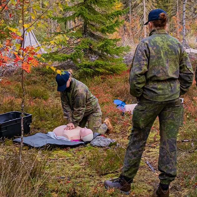 Henkilö elvyttää Anne-nukkea metsässä. Toinen henkilö seuraa vieressä.