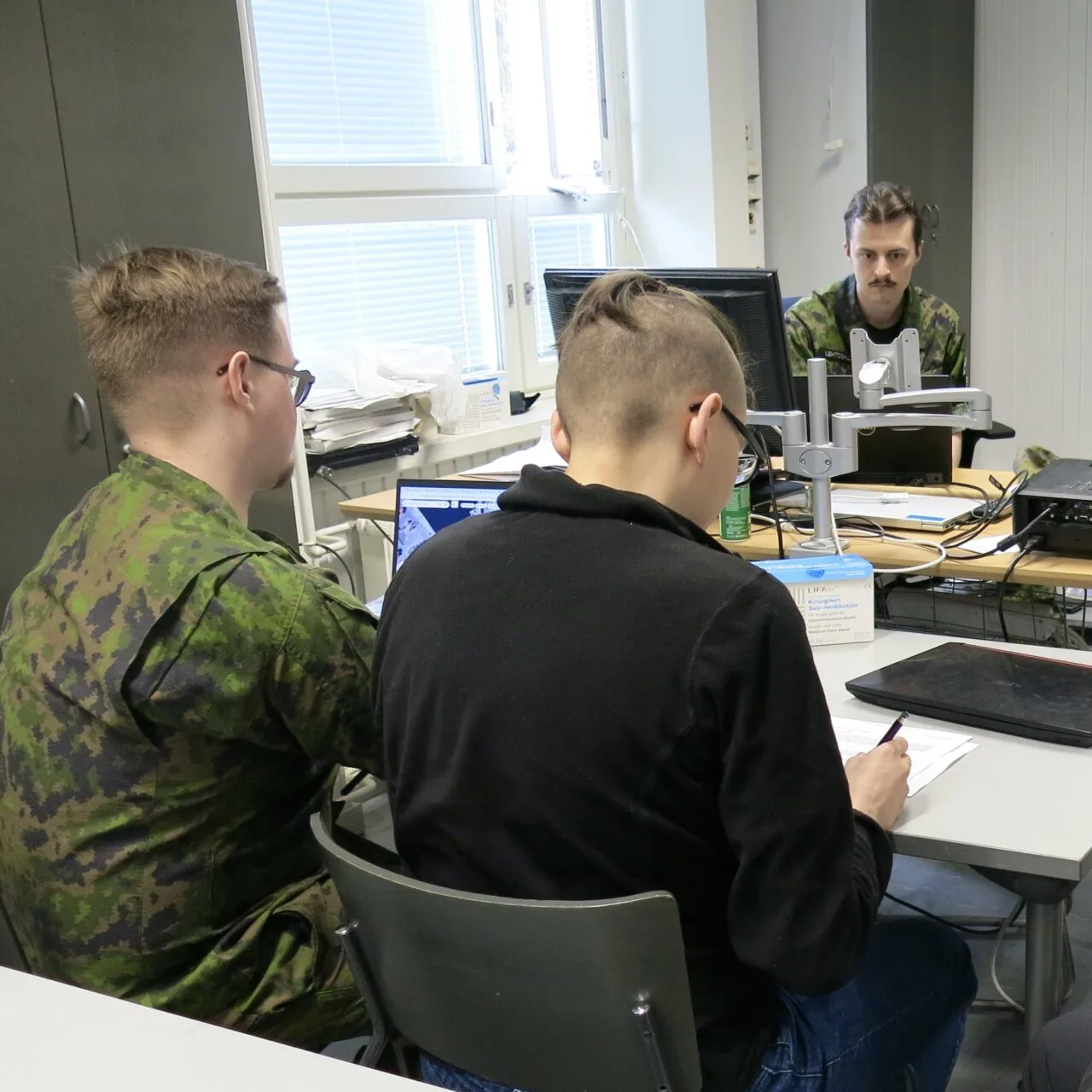 Ryhmä ihmisiä luokkahuoneessa pöydän ääressä.