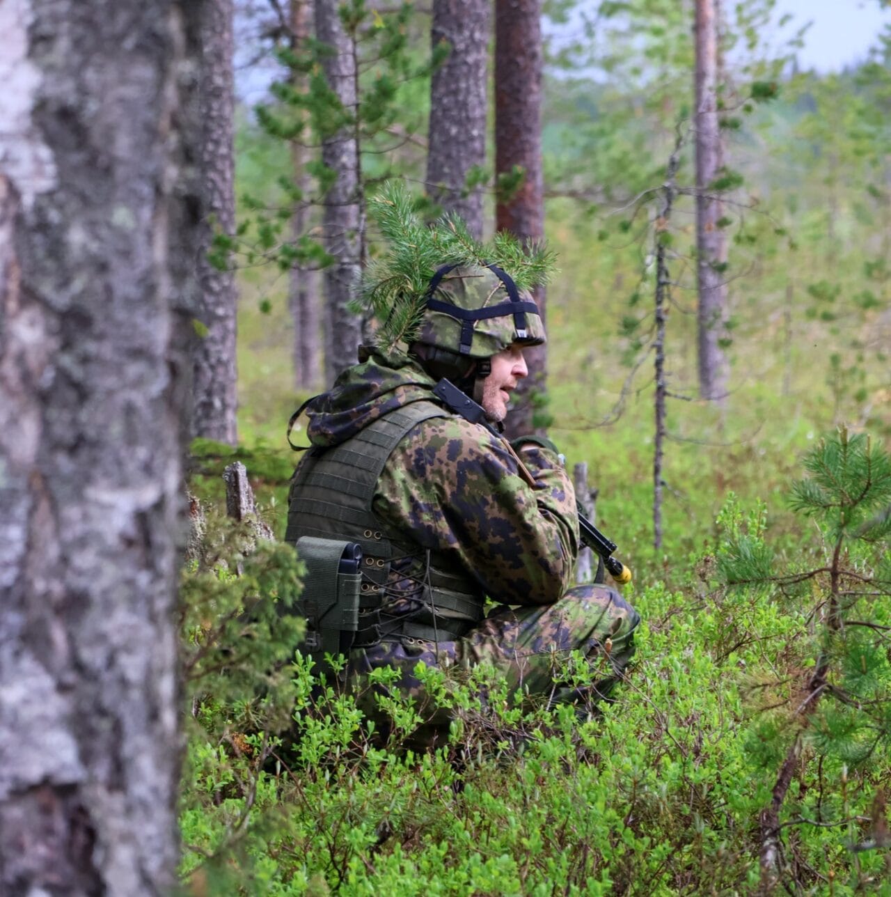 Henkilö istuu metsässä sotilaspuku päällään