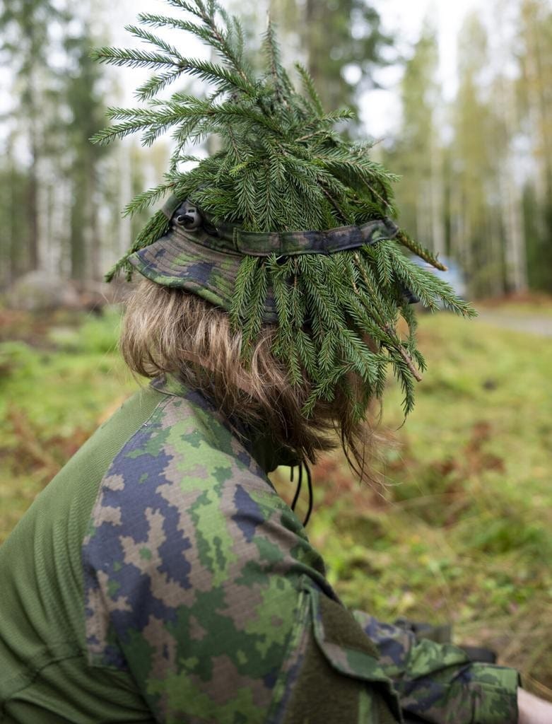 Sivuprofiili sotilaasta, jolla on havuja lierihatussa.