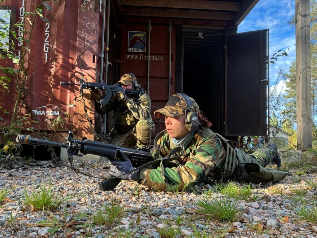 Kaksi henkilöä sotilaspuvuissa ja aseet kädessä väijyvät kontin edessä