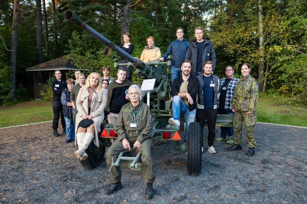 Ryhmäkuva tykin ympärille kokoontuneista ihmisistä, jotka hymyilevät.