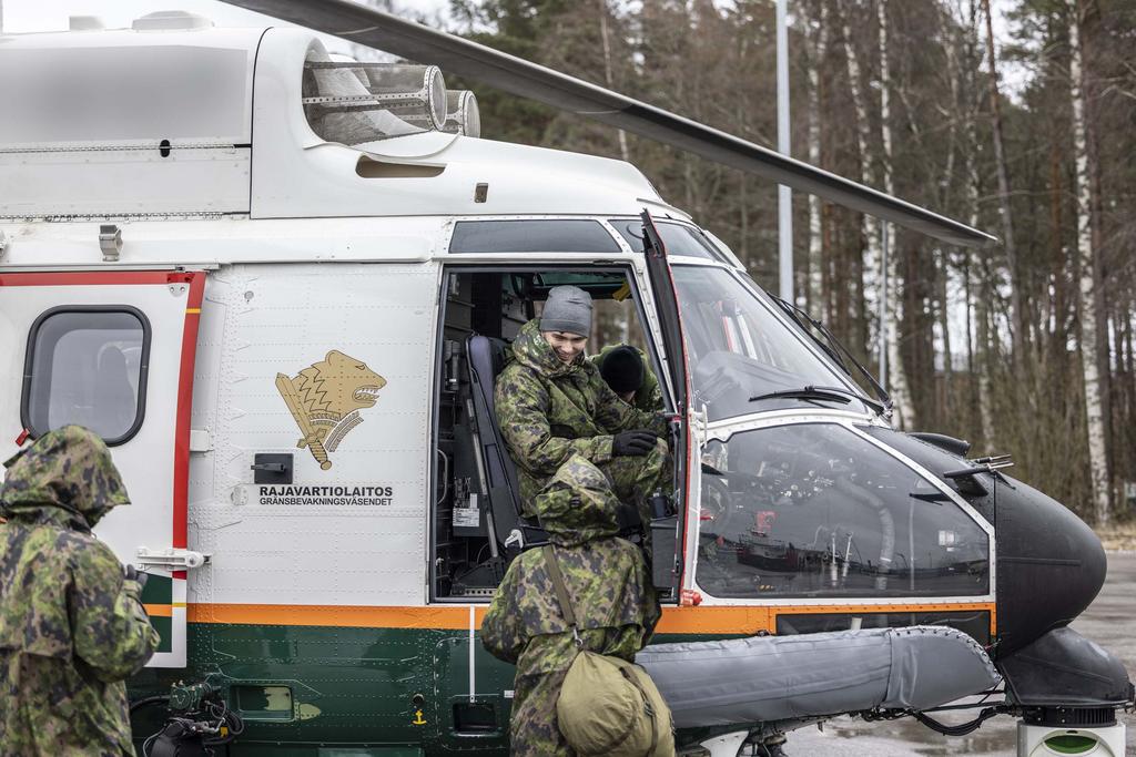 Rajavartiolaitoksen helikopteri kuljettajineen. Kopterin edessä kaksi maastopukuista nuorta.