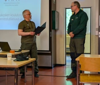 Mies luovuttamassa kunniakirjaa toiselle henkilölle.