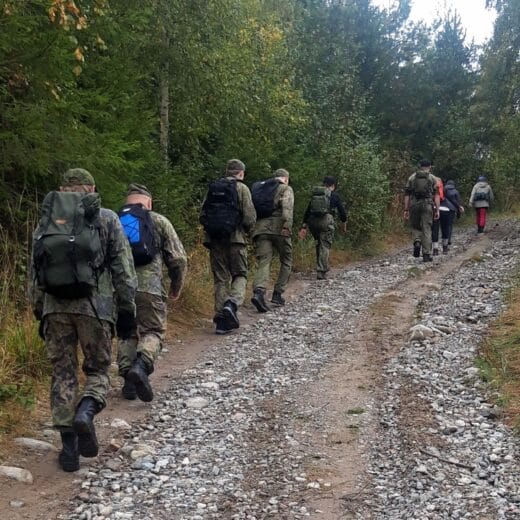 Joukko ihmisiä marssii hiekkatietä poispäin