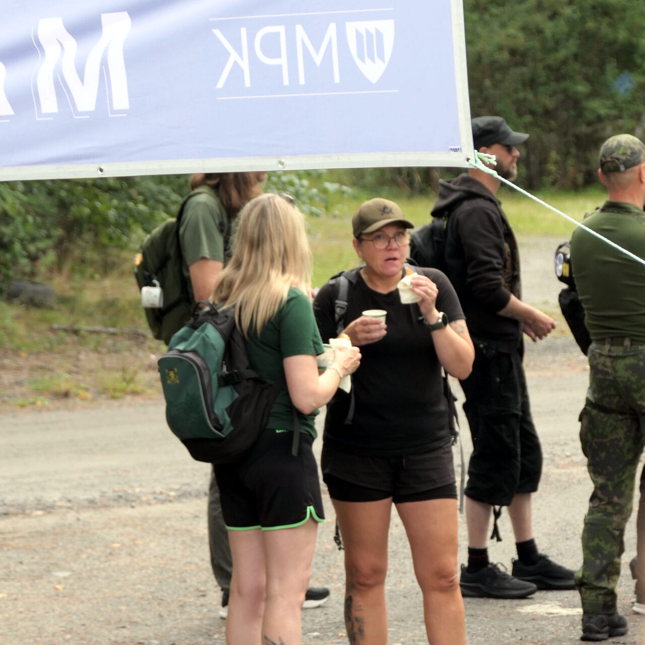 Kuvassa kaksi naista munkkikahvilla maaliintulolipun alla,