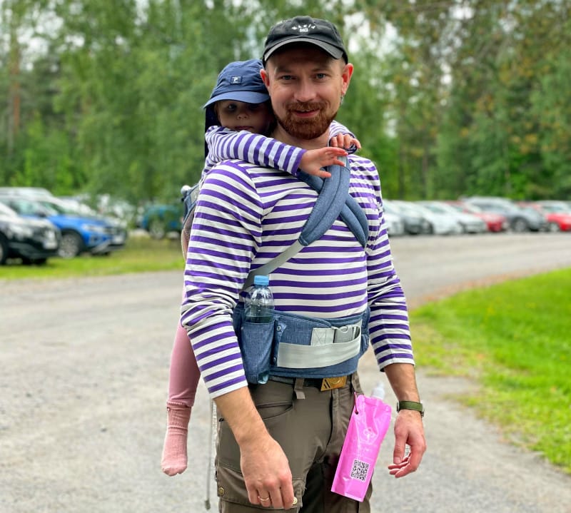 Kuvassa nuori mies, jolla pikkutyttö reppuselässä.