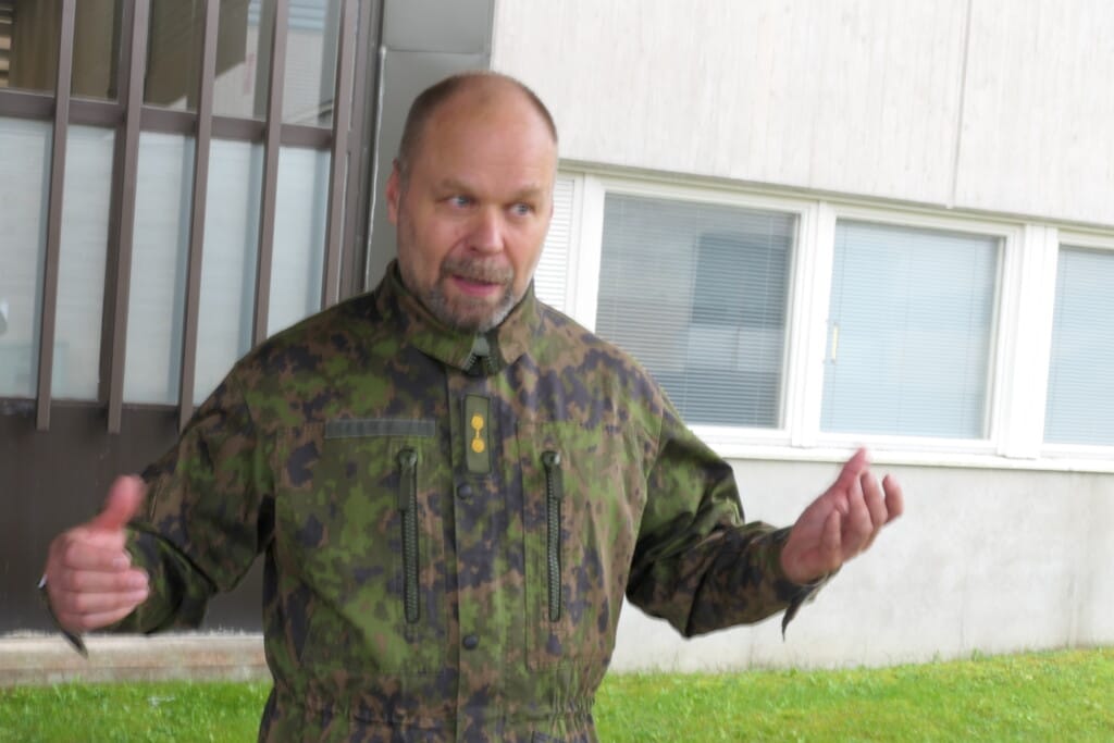 Mies maastopuvussa selittää kädet levällään