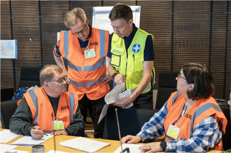 Yksi nainen ja kolme miestä keskustelevat alueellisen valmiuskeskuksen tilannehuoneessa.